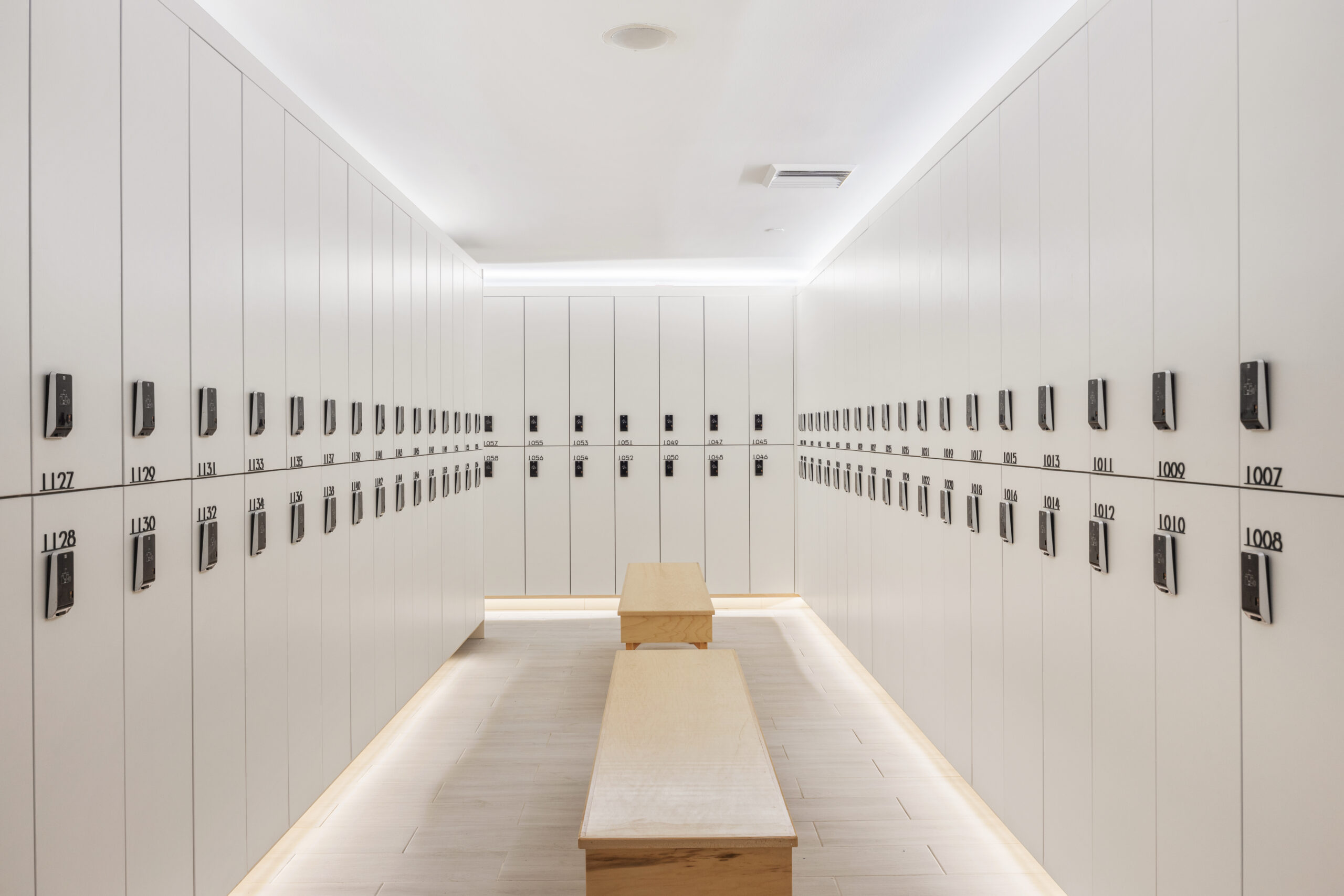inside the locker room isle, featuring benches and closed white lockers.