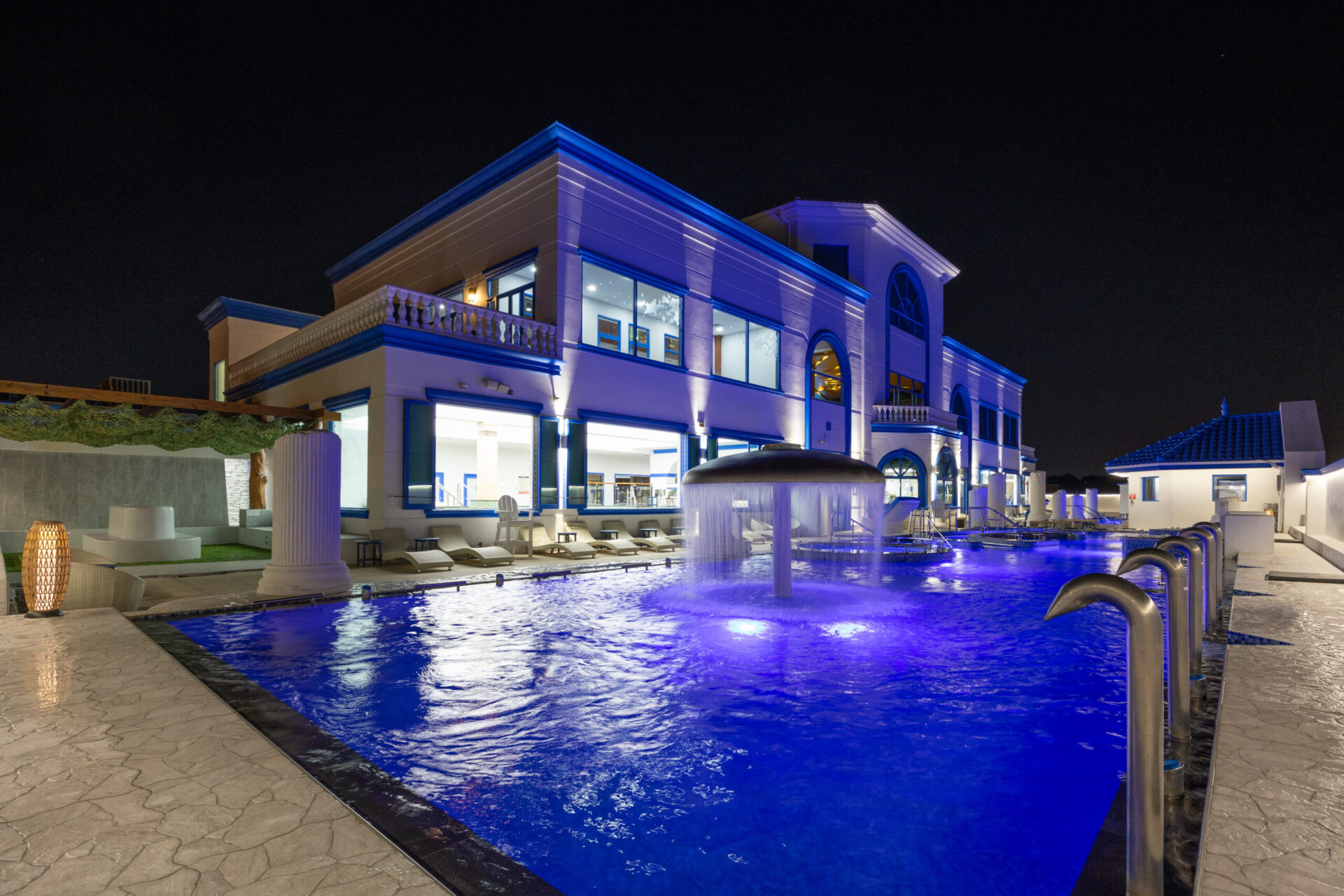 Nighttime of outdoor pool area, with focus of the facility, view of the standing medi pool and waterfall amenity.
