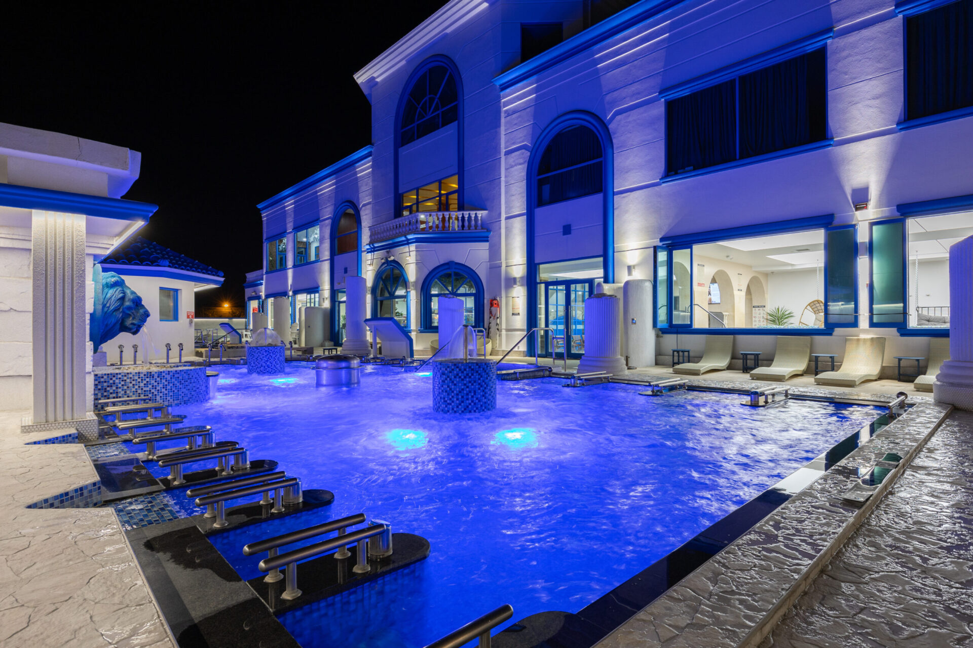 nighttime view of the outdoor pool area, focusing the Spa Castle building, outdoor pool deck, and seated medi pool.